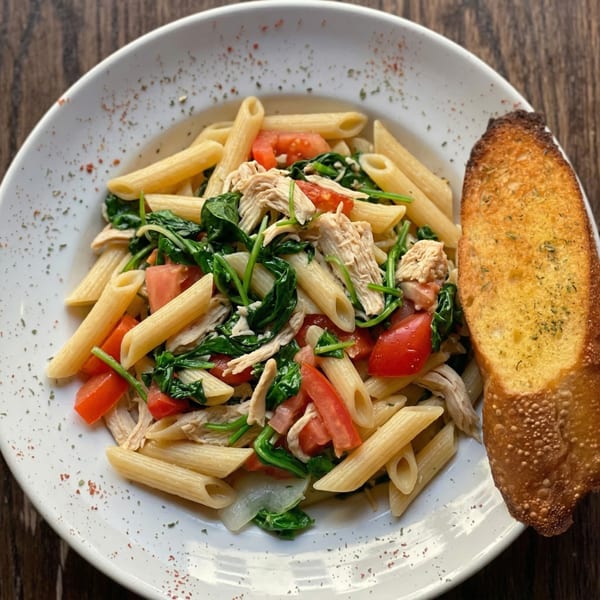 Penne pasta with chicken, spinach, and tomatoes, served with a side of garlic bread.