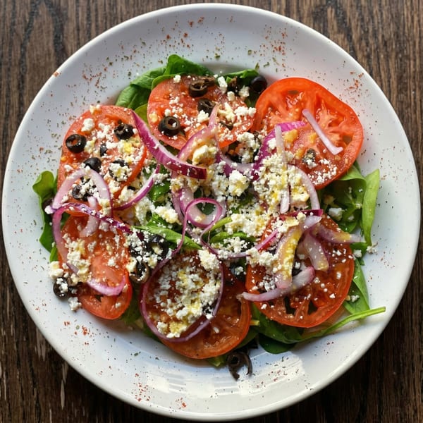 A vibrant salad with spinach, sliced tomatoes, red onions, black olives, and crumbled feta cheese.