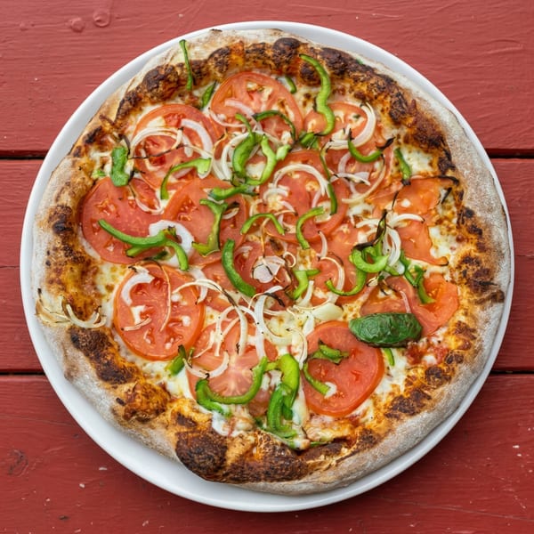 A whole pizza topped with sliced tomatoes, onions, green peppers, and a basil leaf on a white plate.