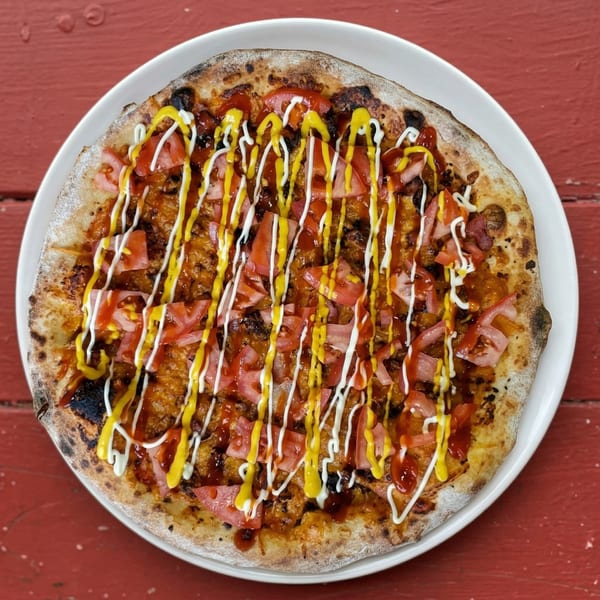 A pizza with diced tomatoes, ketchup, mustard, and mayonnaise drizzle on a white plate.