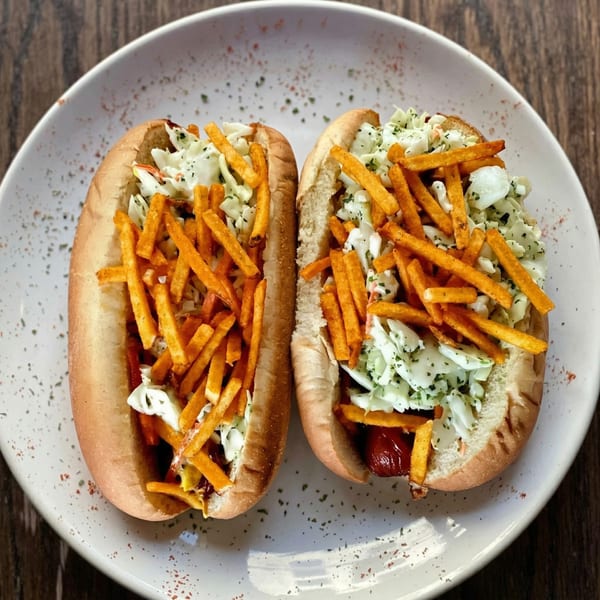 Two hot dogs topped with coleslaw and crispy french fries on a white plate.